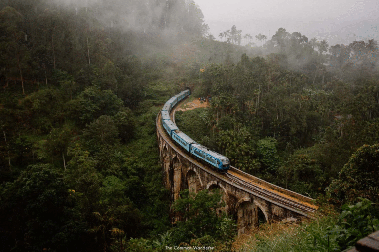 Blue train crossing the iconic Nine Arches Bridge in Ella, Sri Lanka, surrounded by lush green forest and morning mist.