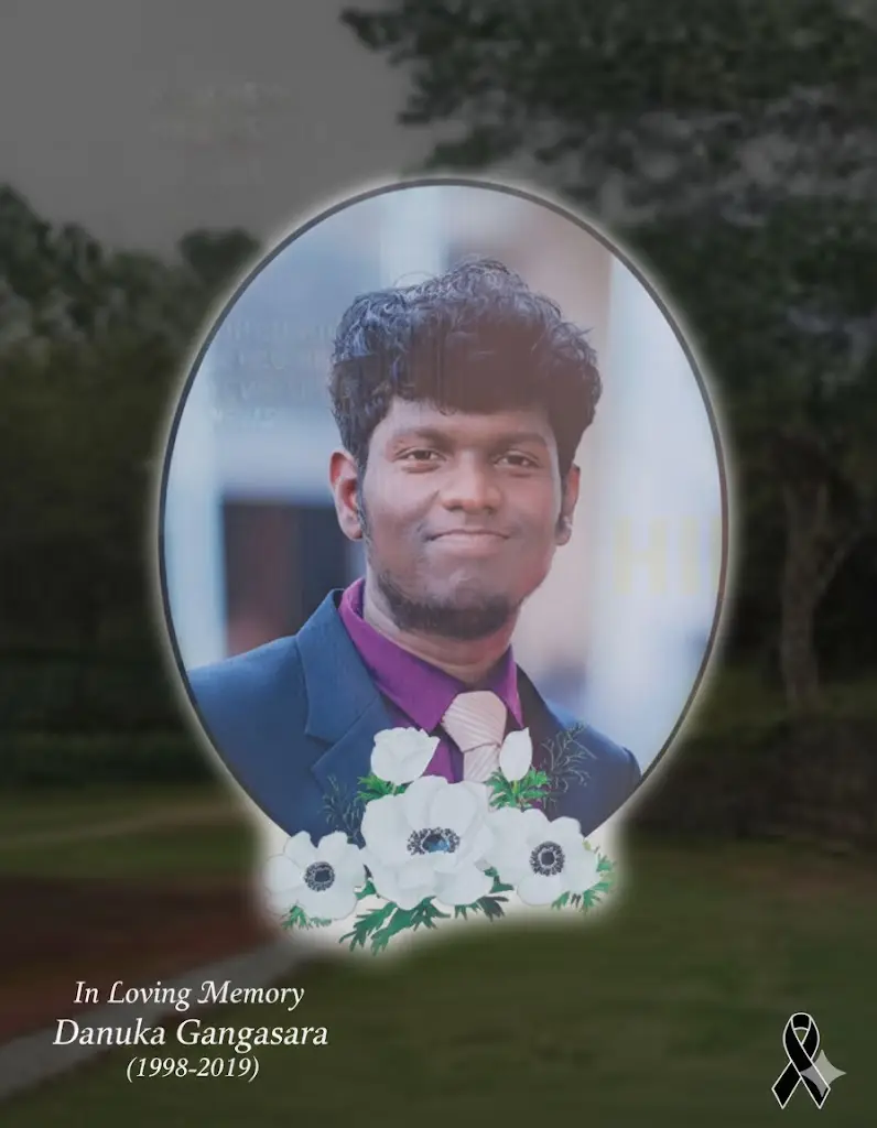 Commemorative feature image for the article: A portrait of Danuka Gangasara, a smiling young man in a dark suit and purple shirt, set in an oval frame with white memorial flowers, and the text "In Loving Memory - Danuka Gangasara (1998-2019)" overlaying the bottom corner.